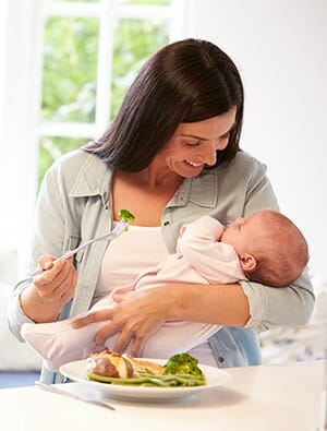 New mother holding her newborn eating a healthy dinner