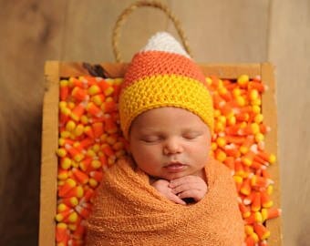 swaddled newborn baby wearing candy corn hat