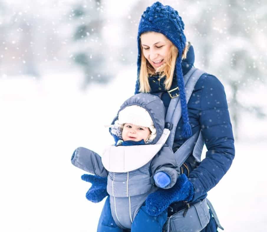 mom bundled with baby in the snow playing