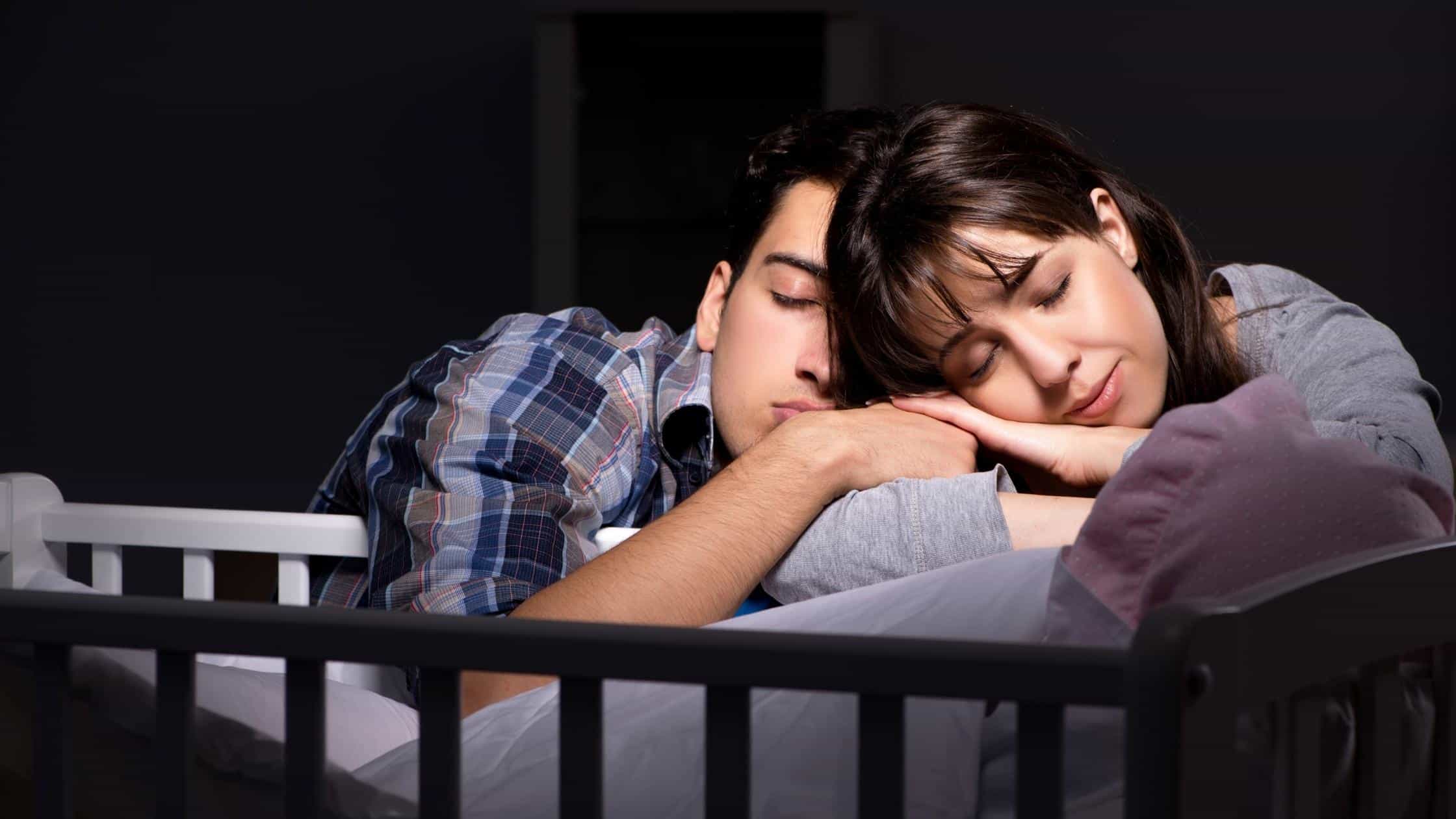 parents asleep on baby crib with baby