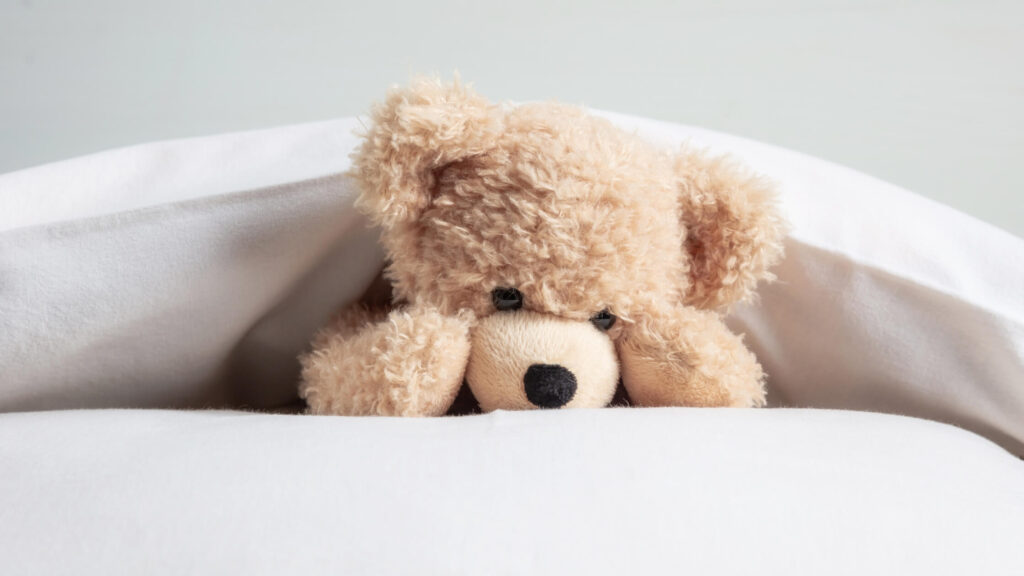 teddy bear tucked into a bed