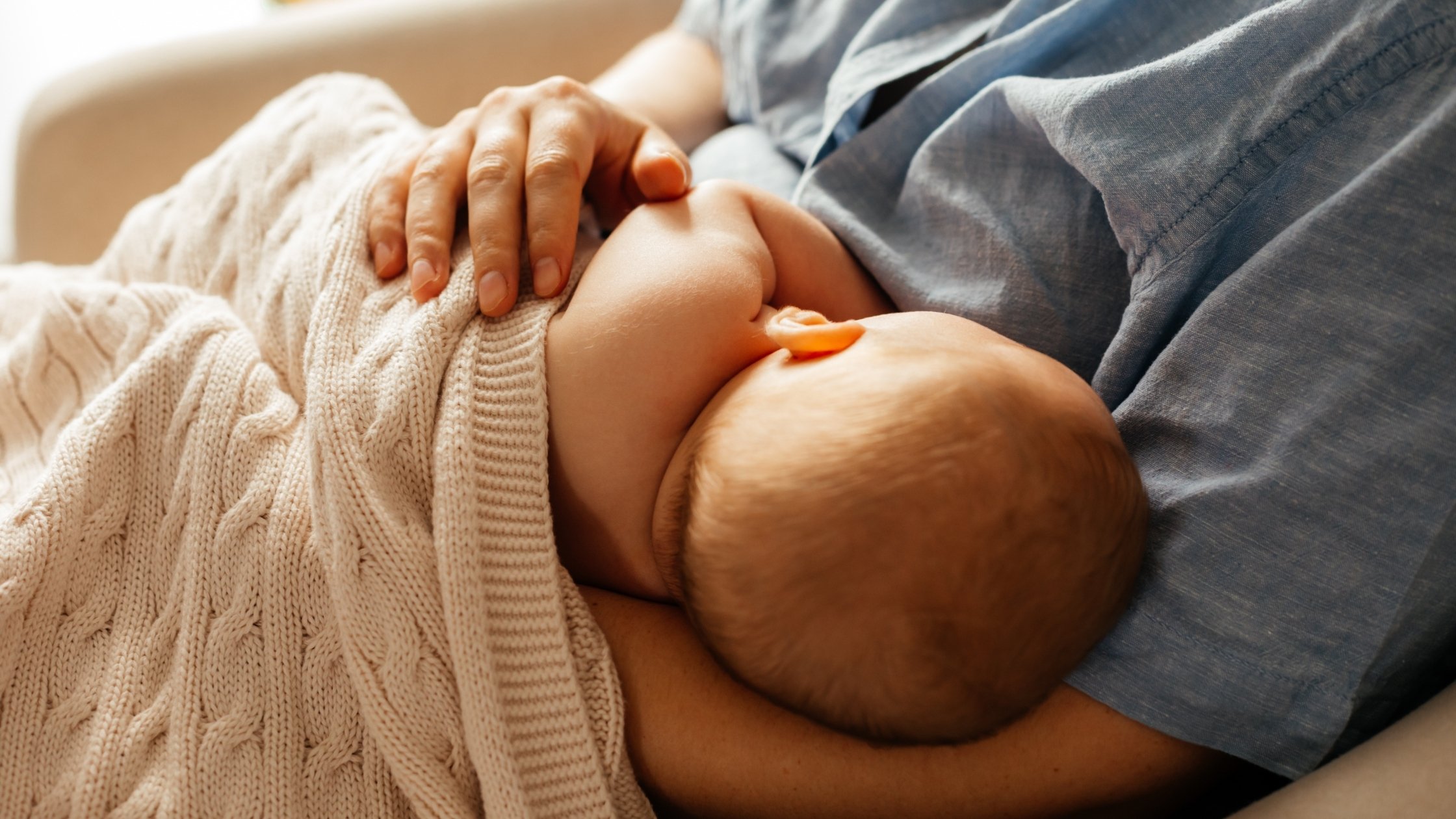 woman in blue shirt breastfeeding a newborn baby