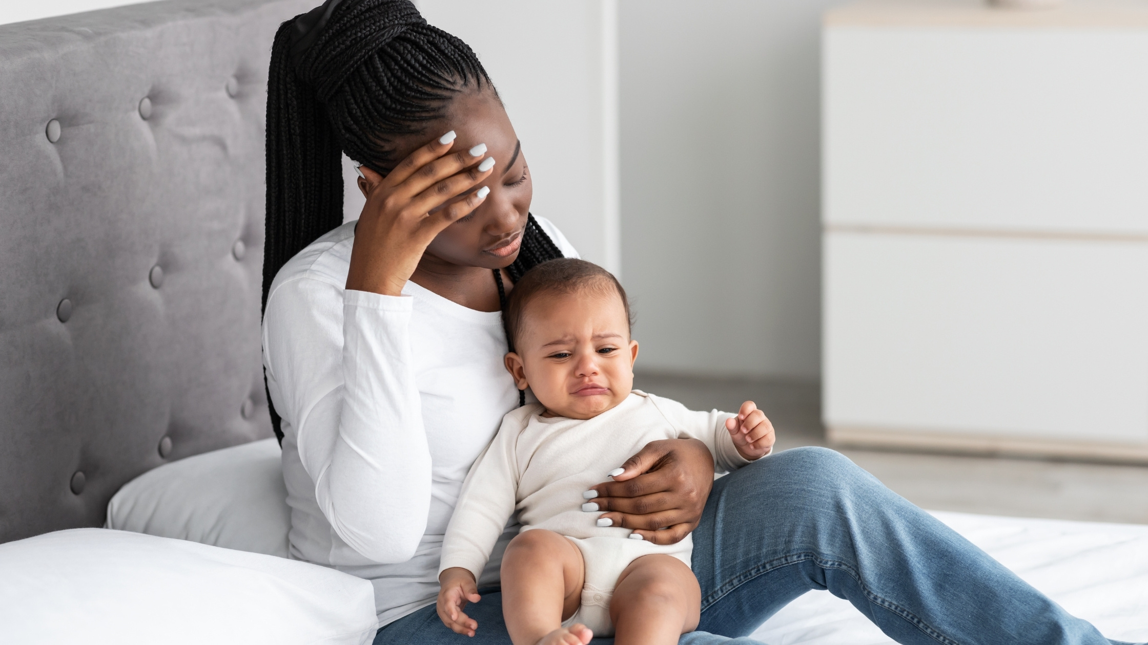 woman on bed holding baby with headache