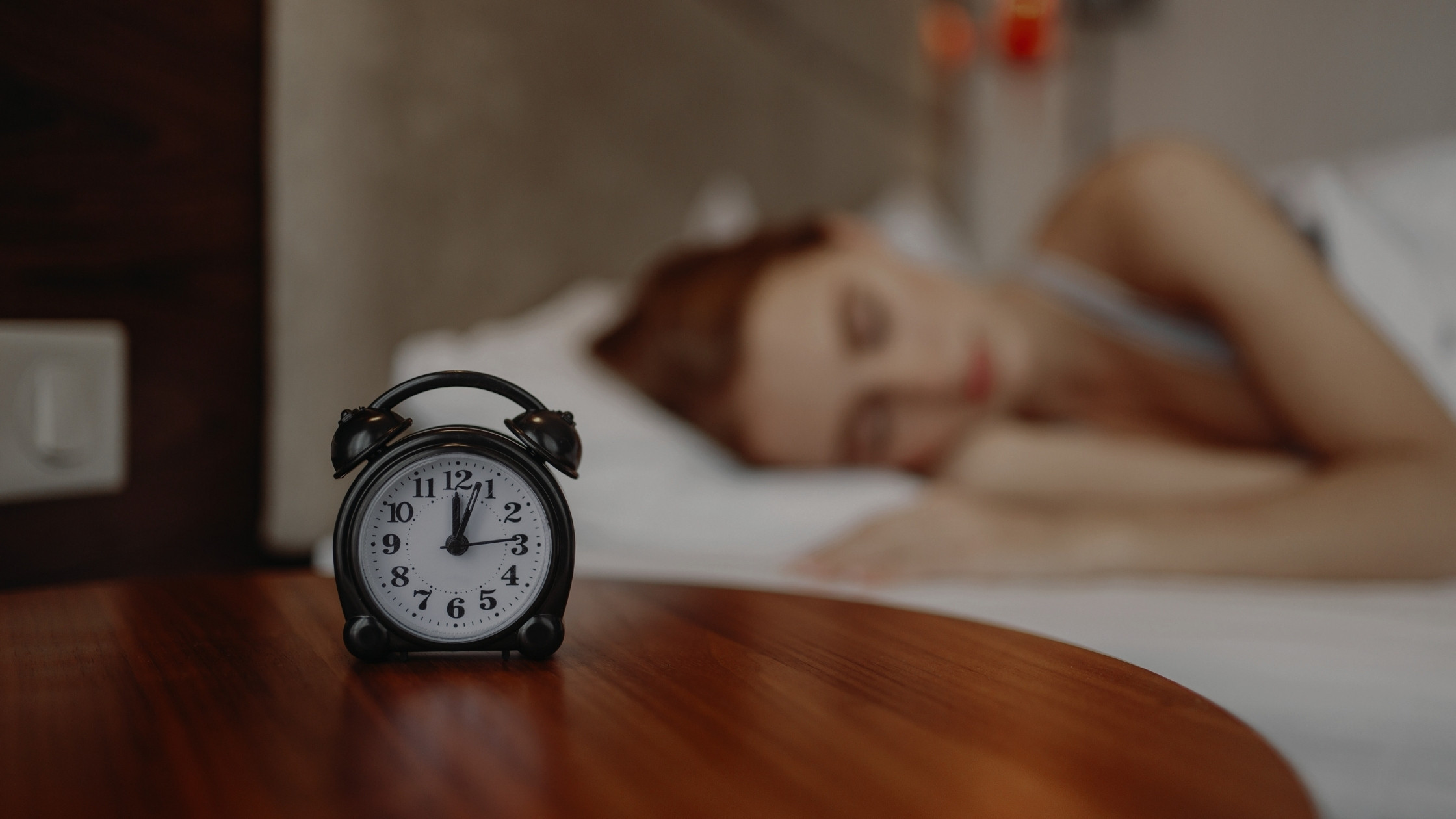 woman sleeping with alarm clock in foreground