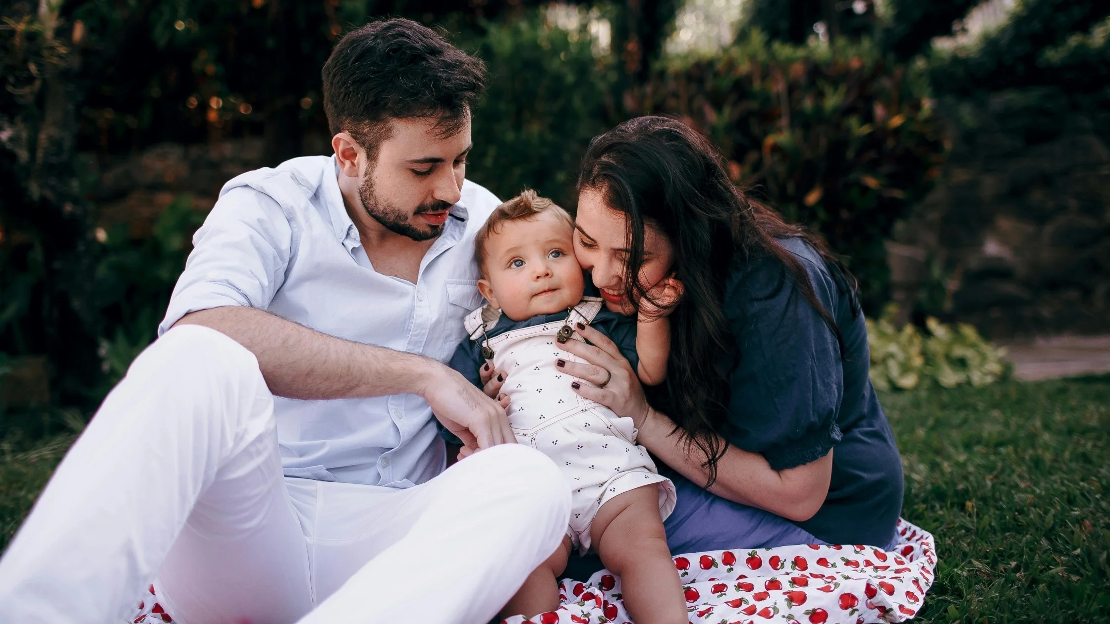 a baby and her parents sitting on the grass