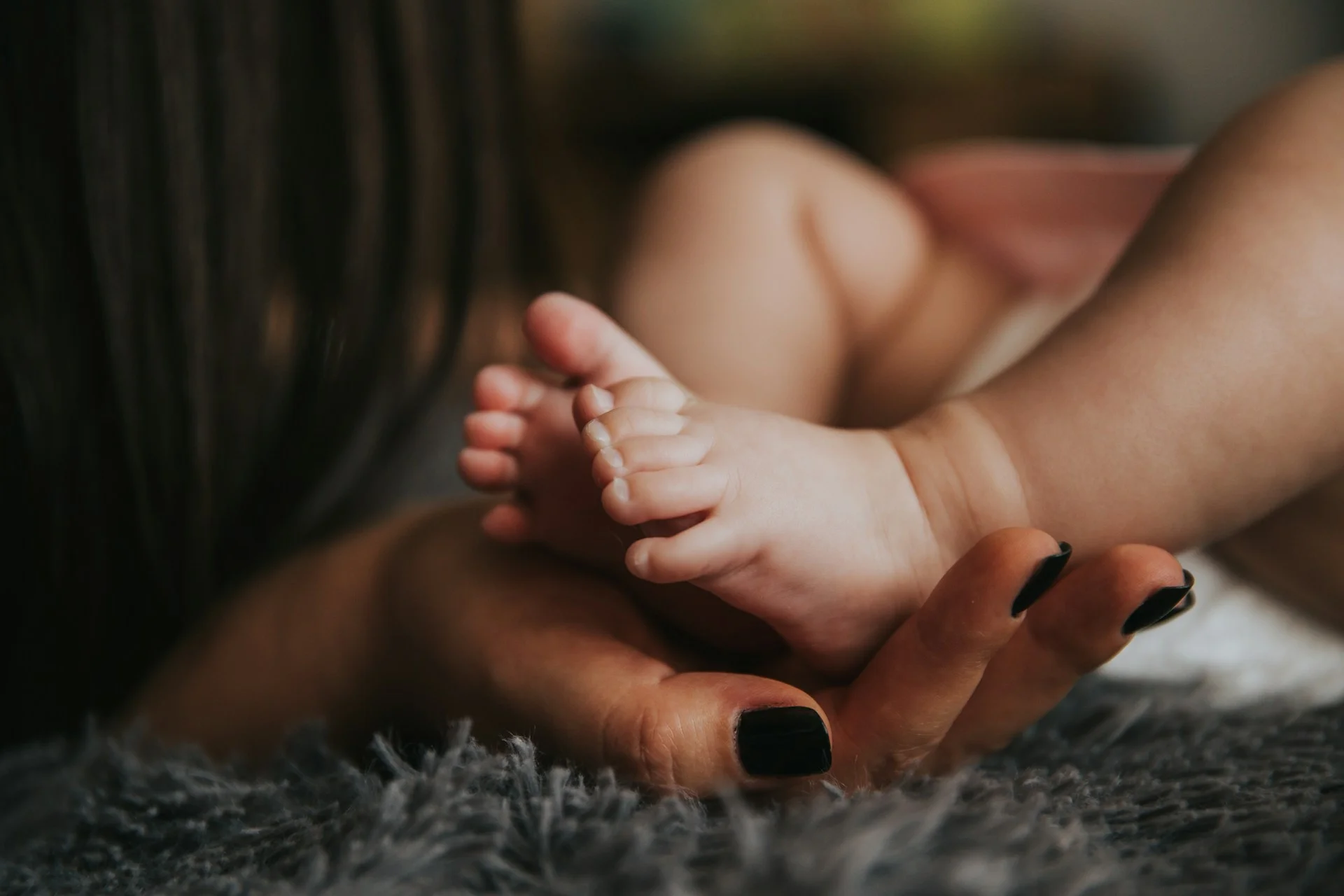 a baby laying on a grey blanket with its feet being held by its mother